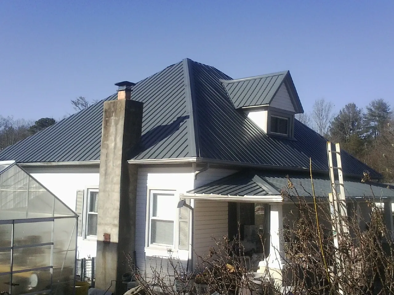 Dark blue standing seam metal roof on a white farmhouse with dormer — Slate & Tile Roof Repair by Roofing Brothers in Oneida