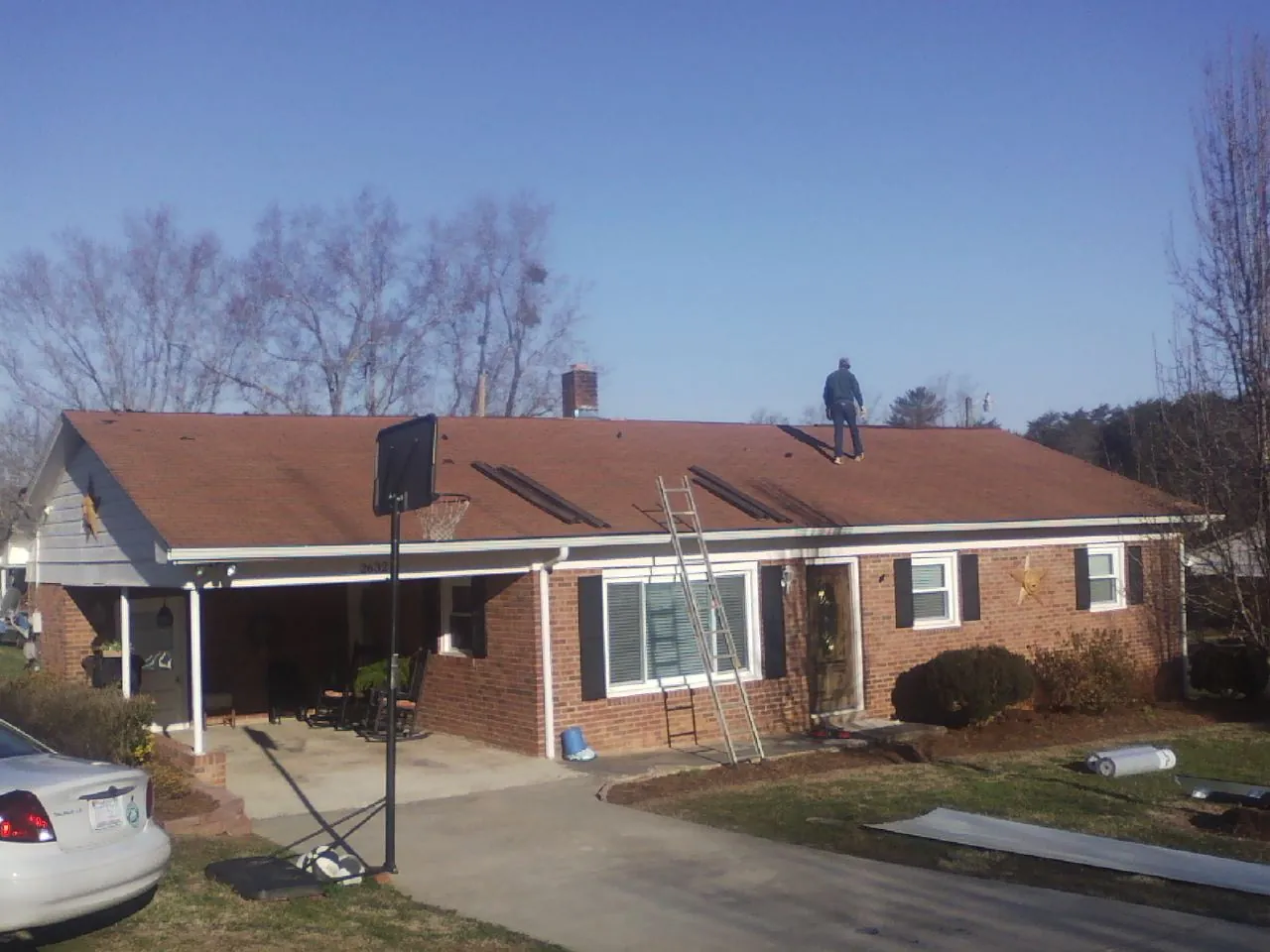 Roofer stripping a shingle roof on a brick ranch before metal panels in Oneida