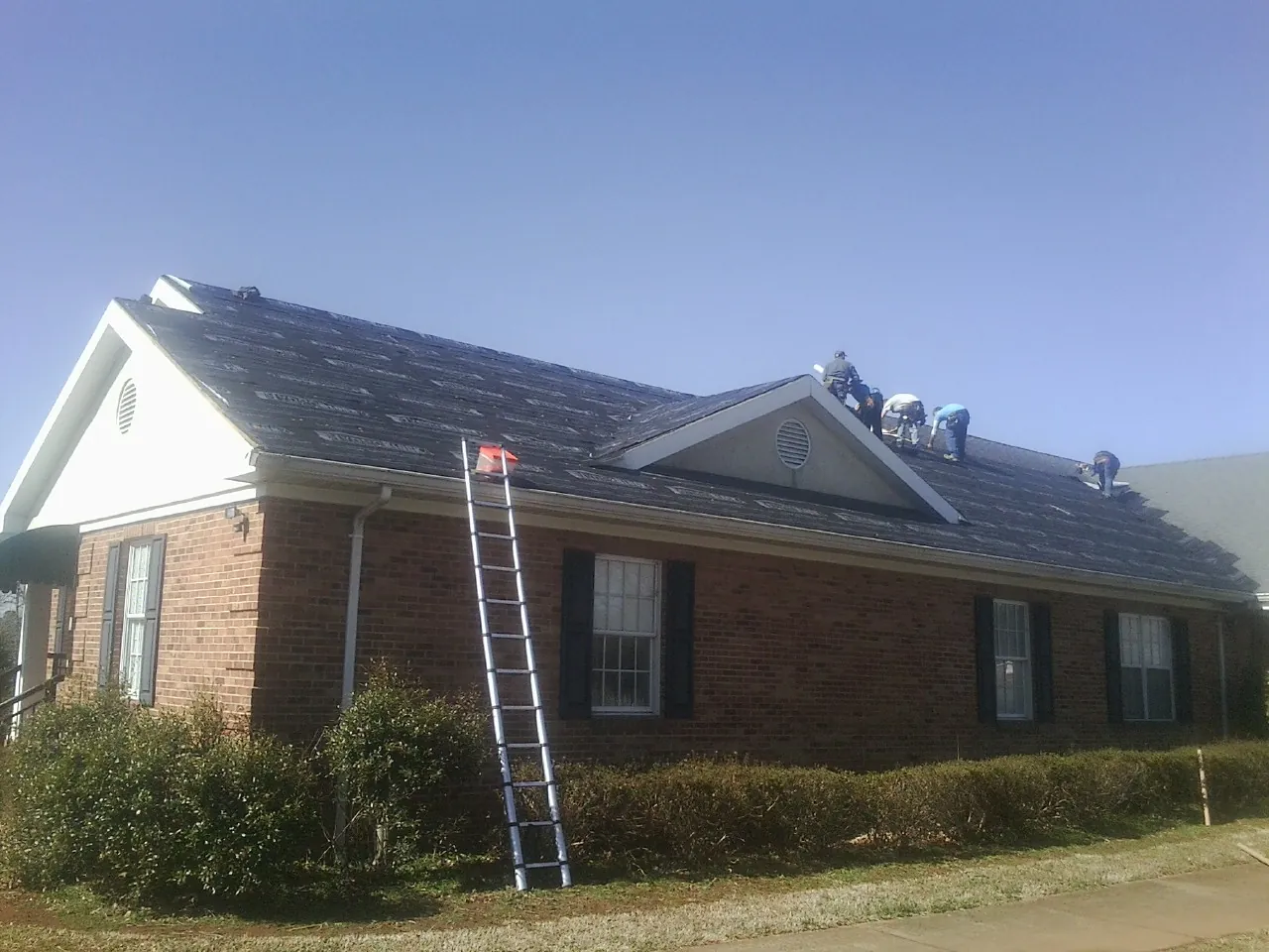 Crew tearing shingles off a brick ranch roof with a ladder set — Emergency Roof Repair work by our crew in Oneida