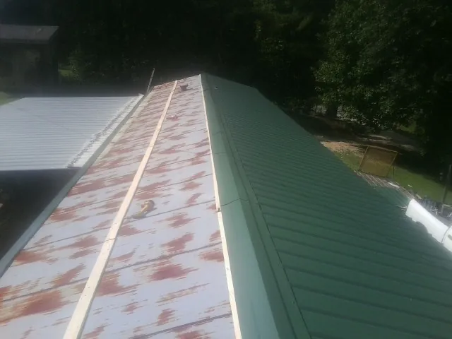 Old rusted panels beside newly installed green metal roofing — Wind Damage Roof Repair by Roofing Brothers in Oneida