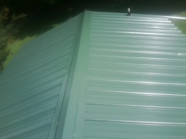 New green metal panels meeting at the ridge of a roof — Flat Roof Repair work by our crew in Oneida