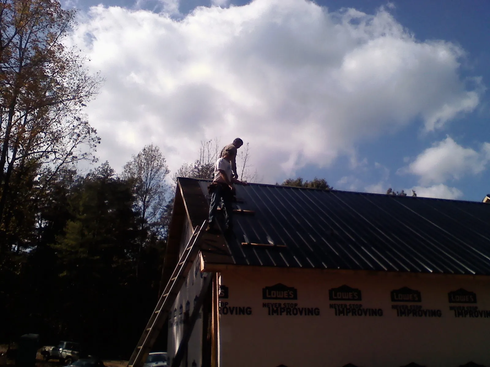 Roofer fastening dark metal panels high against a cloudy sky, from a Roof Inspection job in Oneida