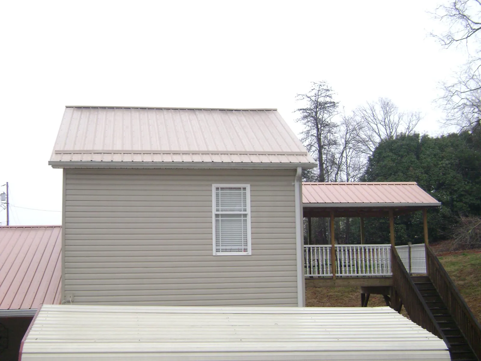Tan metal roofs on a two story addition and attached porch, from a Roof Replacement job in Oneida